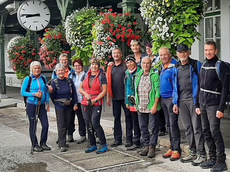 Wandergruppe vor einem Bahnhof mit Blumenschmuck